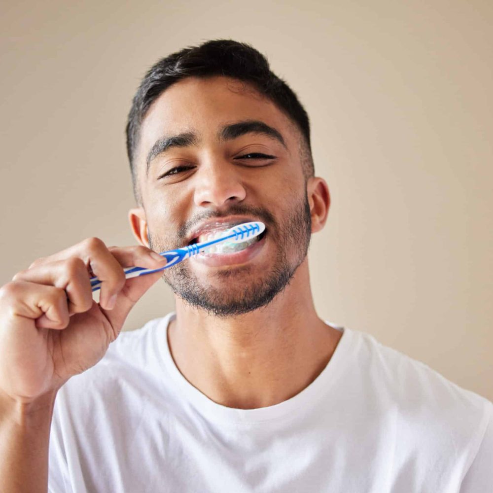 Studio shot of a handsome young man brushing his teeth against a studio background.